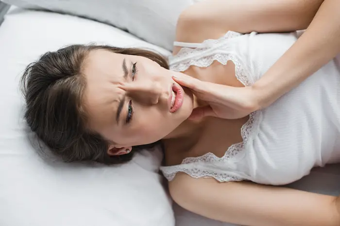 woman suffering from tooth pain while lying in bed
